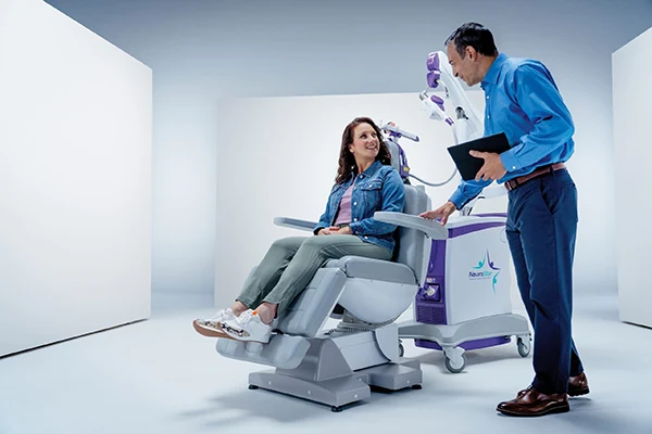 Patient seated in the NeuroStar treatment chair while a clinician prepares the session