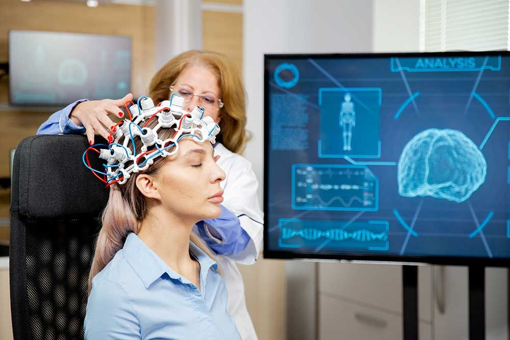 Woman wearing an EEG sensor cap beside a screen showing brain activity